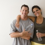 Man and woman at gym in fitness attire holding water bottles sta